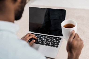Afrika kökenli Amerikalı adam laptop ve holding fincan çay kullanarak