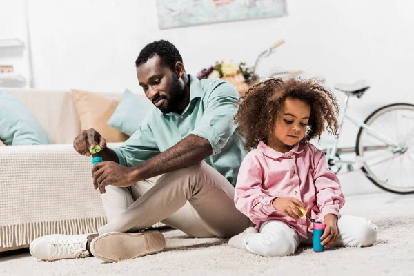 非洲裔美国的父亲和女儿坐在地板上 制造肥皂泡 向下看 — 图库照片