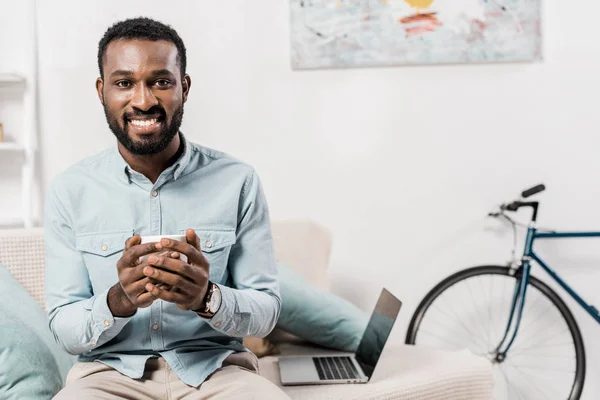 Sonriente Afroamericano Freelancer Sosteniendo Taza Sentado Sofá Sala Estar — Foto de stock gratis