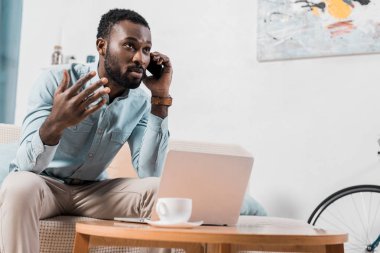 Afro-Amerikan freelancer kanepede otururken Smartphone'da konuşuyor