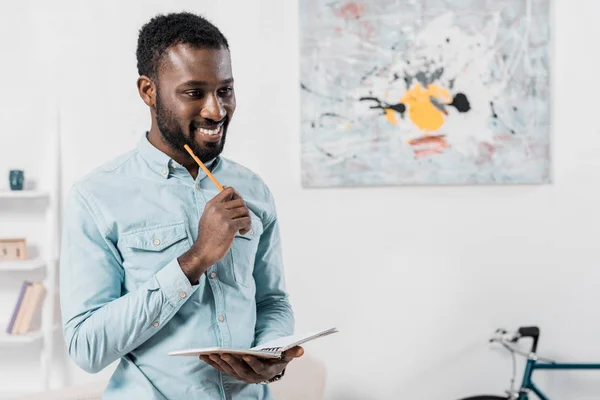 Усміхнений Афроамериканський Чоловік Тримає Олівець Блокнот — Безкоштовне стокове фото