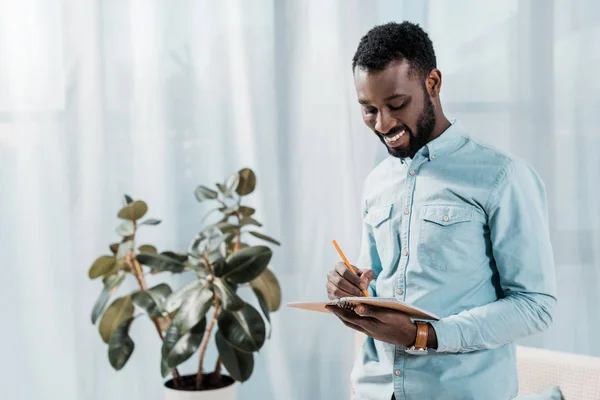 Lächelnder Afrikanisch Amerikanischer Mann Schreibt Notizblock — Stockfoto