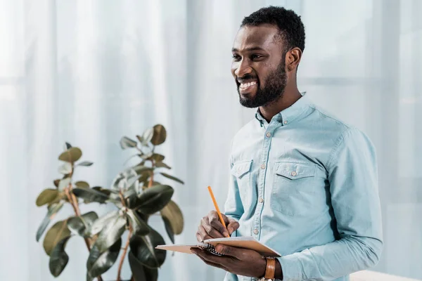 Handsome African American Freelancer Writing Notepad Looking Away — Free Stock Photo