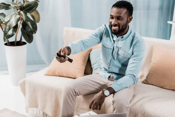 Усміхнений Афроамериканський Чоловік Сидить Дивані Використовує Пульт Дистанційного Керування — Безкоштовне стокове фото