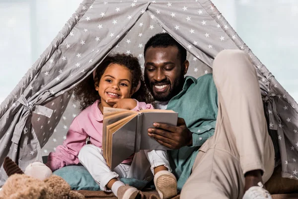 Afrikaanse Amerikaanse Vader Lezen Boek Met Kind Glimlachend Woonkamer — Stockfoto