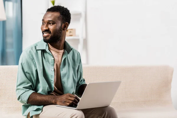 African American Man Using Laptop Knees Looking Away Living Room — Free Stock Photo