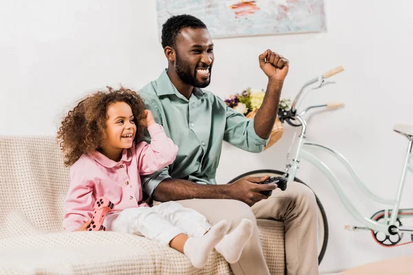 african american dad and daughter playing video game in living room