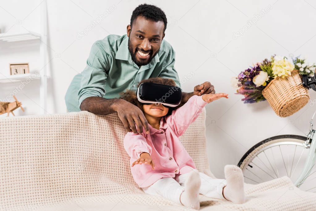 african american man showing daughter virtual reality glasses in living room