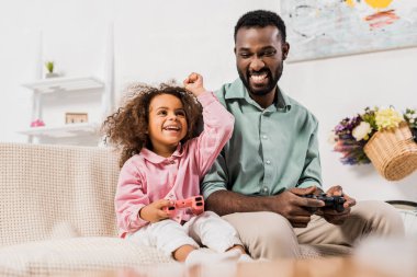 Afro-Amerikan baba ve kız oturma odasında oyun çubukları ile bilgisayar oyunu oynamak