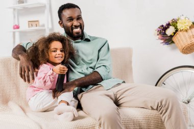 Afrika kökenli Amerikalı adam ve kızı oturma odasında televizyon izlerken