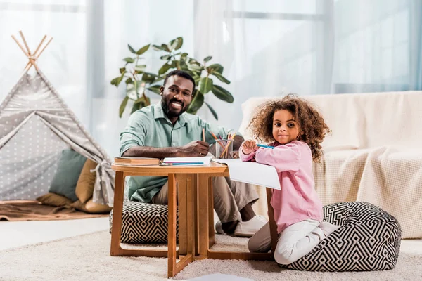 Africano Americano Papà Aiutare Figlia Con Disegno Guardando Fotocamera Soggiorno — Foto Stock