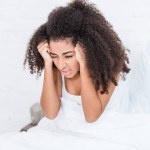 Selektiver Fokus einer jungen Afroamerikanerin, die zu Hause Kopfschmerzen im Bett hat Selektiver Fokus einer jungen Afroamerikanerin, die zu Hause Kopfschmerzen im Bett hat