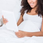 Partial view of african american curly woman using digital tablet in bed at home