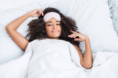 evde yatakta döşeme sırasında kameraya arıyor alnı göz bağını olan Afrika kökenli Amerikalı kadın portresi