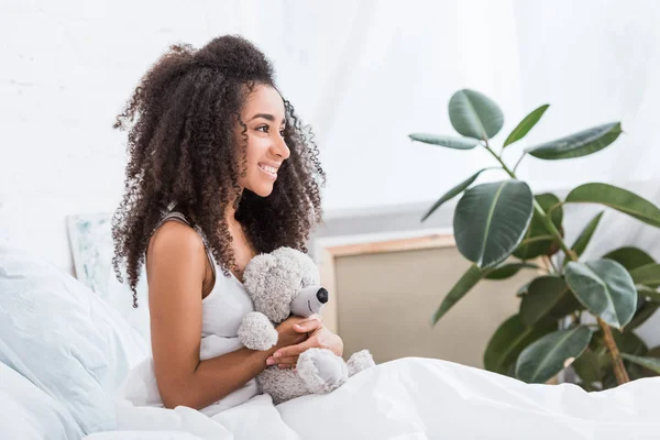 Sidovy Leende African American Curly Flicka Sängen Med Teddybjörn Hemma — Gratis stockfoto