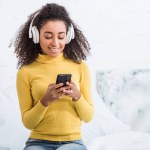 Atractiva joven en auriculares escuchando música con teléfono inteligente en casa