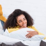 Rêveuse belle afro-américaine jeune femme couchée au lit et regardant loin