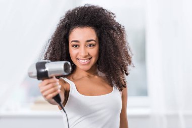 neşeli güzel Afro-Amerikan Kız evde saç kurutma makinesi holding
