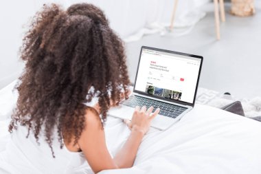 Dikiz airbnb evde yatakta ekranda ile dizüstü bilgisayar kullanan kıvırcık kadın