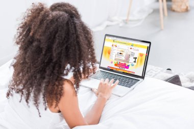 Dikiz aliexpress evde yatakta ekranda ile dizüstü bilgisayar kullanan kıvırcık kadın