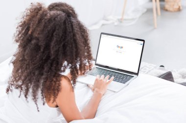 evde yatakta ekranda google ile dizüstü bilgisayar kullanan kıvırcık kadın dikiz