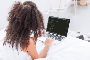 evde yatakta ekranda kod programlama ile dizüstü bilgisayar kullanan kıvırcık kadın dikiz