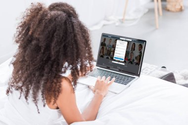 evde yatakta ekranda LinkedIn ile dizüstü bilgisayar kullanan kıvırcık kadın dikiz