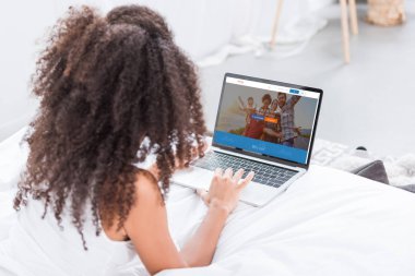Dikiz couchsurfing evde yatakta ekranda ile dizüstü bilgisayar kullanan kıvırcık kadın