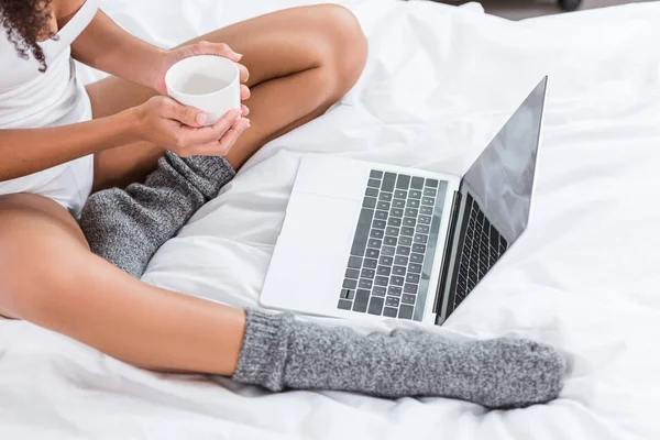早上在家的时候 在床上用带空白屏幕的笔记本电脑的女人拿着咖啡杯的照片 — 免费的图库照片