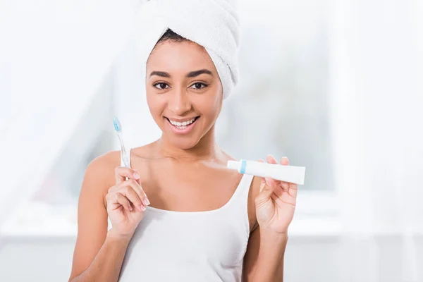 タオルでうれしそうなアフリカ系アメリカ人の若い女性ラップ以上頭を示す歯磨き粉 歯ブラシ — ストック写真