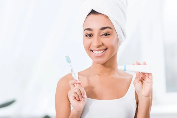 タオルで肯定的なアフリカ系アメリカ人の若い女性ラップ以上頭を示す歯磨き粉 歯ブラシ — ストック写真