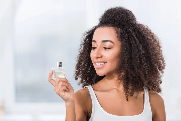 快乐的非洲裔美国人卷曲的女孩使用香水在家里 — 免费的图库照片