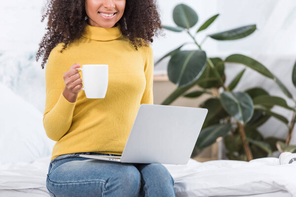 partial view of female freelancer with coffee cup working on laptop at home