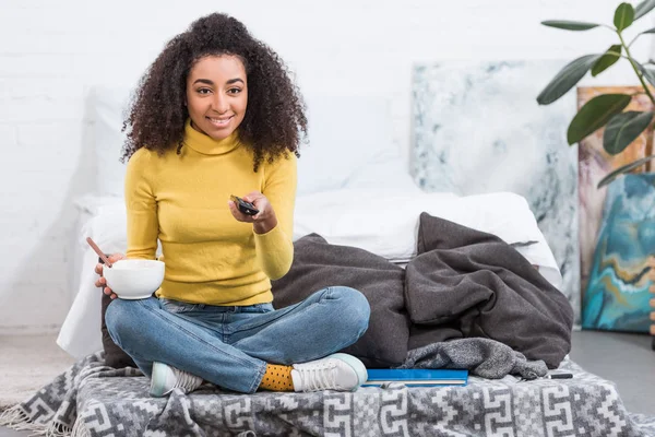 Chica Afroamericana Bastante Elegante Sosteniendo Tazón Con Comida Viendo Televisión — Foto de Stock