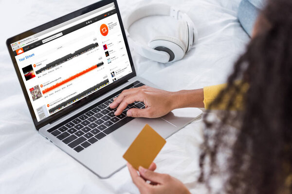 cropped image of woman holding credit card and using laptop with soundcloud on screen