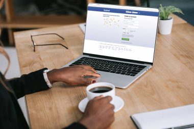 Afrikalı-Amerikalı kadın kahve yakınındaki Web sitesi facebook ile dizüstü bilgisayar kullanarak kırpılmış görünümünü