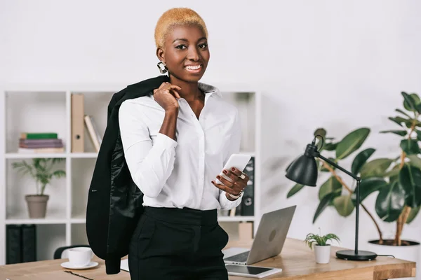 Afrikanisch Amerikanische Geschäftsfrau Mit Kurzen Haaren Hält Smartphone Und Jacke — kostenloses Stockfoto
