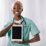 Lachende Afrikaanse Amerikaanse verpleegster met stethoscoop holding digitale tablet met leeg scherm