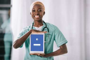 Afro-Amerikan hemşire dijital tablet facebook app ile tutarak stetoskop ile gülümseyen