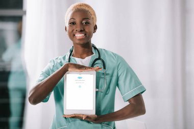 Dijital tablet skype uygulaması ile tutarak stetoskop ile çekici neşeli Afro-Amerikan hemşire