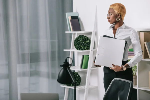 自信的非洲裔美国女商人持有文件夹在现代办公室 — 免费的图库照片