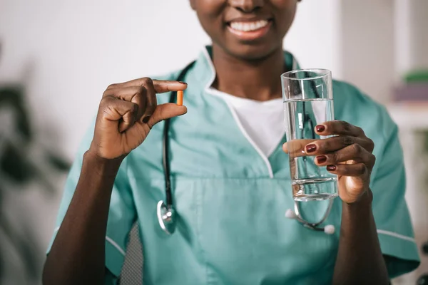 Recortado Vista Sonriente Enfermera Afroamericana Con Estetoscopio Celebración Píldora Vaso — Foto de stock gratis