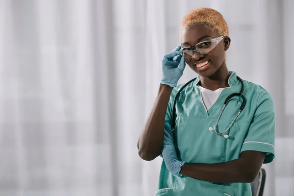 Smiling African American Nurse Gloves Holding Goggles While Looking Camera — Free Stock Photo