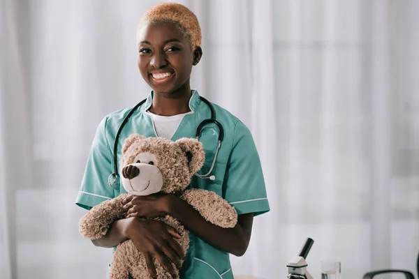 Alegre Afro Americano Enfermeira Segurando Ursinho Pelúcia Clínica Leve — Fotografia de Stock