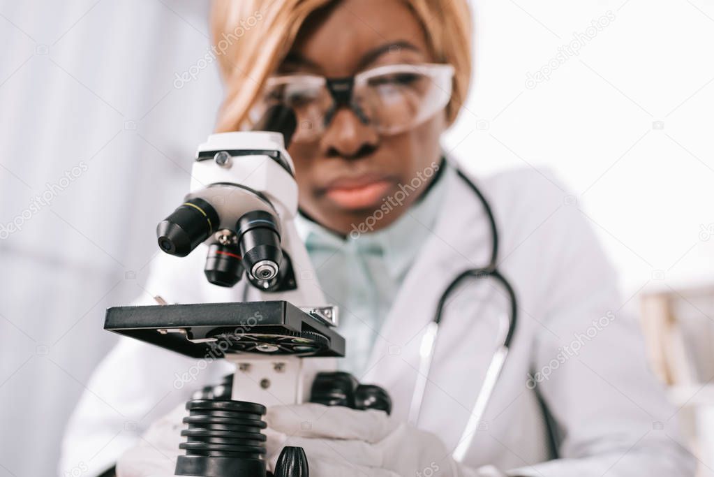 selective focus of microscope with female african american scientist on background