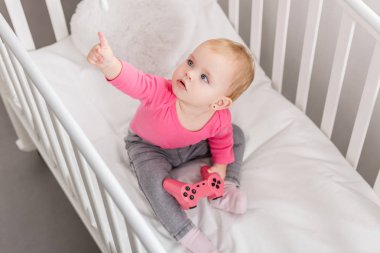 pembe gömlekli beşik ve oyuncağın üstüne işaret pembe oyun çubuğu tutan çok güzel çocuğun yüksek açılı görünüş