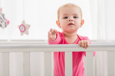 çok güzel çocuk yatağına ayakta ve el kamera için ulaşan pembe gömlekli