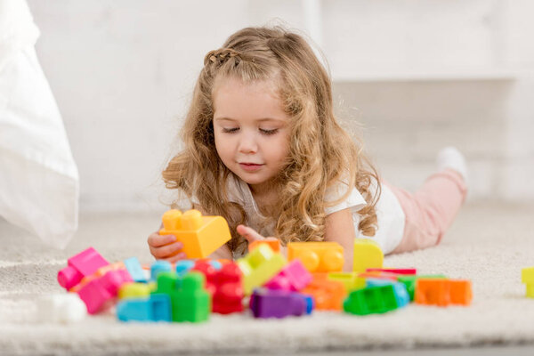 уровень поверхности очаровательного ребенка, играющего с цветным пластиковым конструктором на ковре в детской комнате
