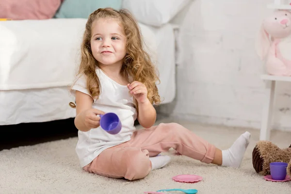 子供部屋で床にプラスチック製のコップで遊ぶ愛らしいキッド — ストック写真