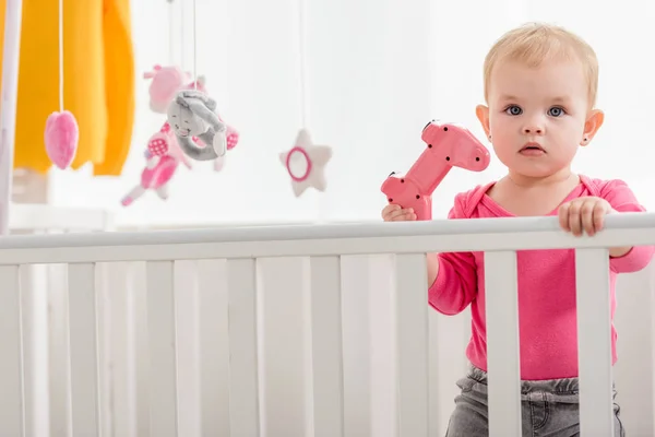Adorable Kid Pink Shirt Holding Pink Joystick Crib Looking Camera — Free Stock Photo